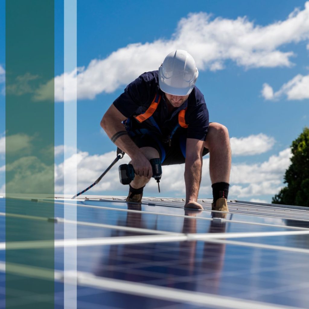 A worker in safety gear using a drill on solar panels